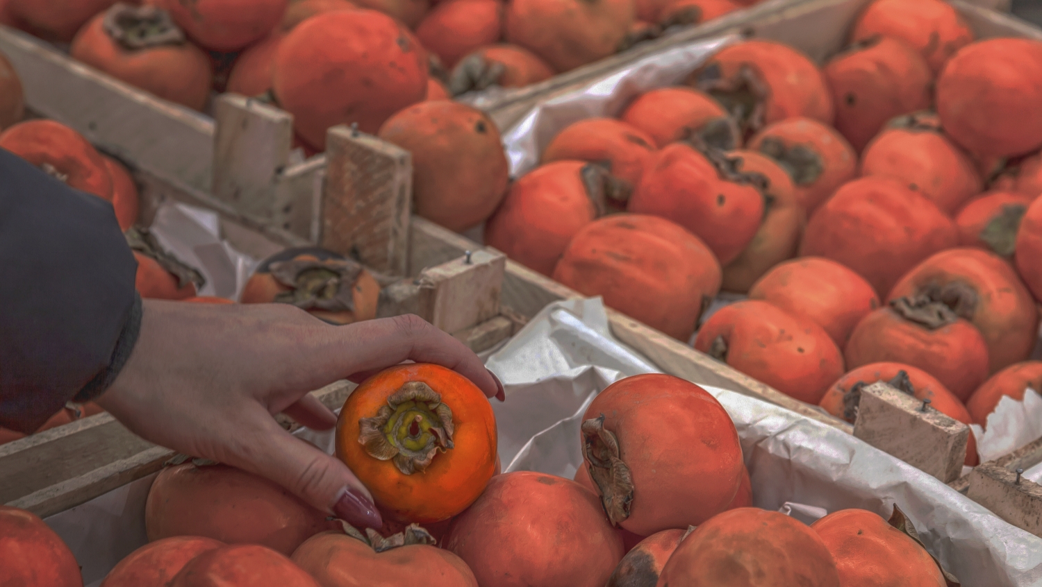 A young girl chooses food while shopping in a mall in the fruit department holding an ripe persimmon of bright orange color in her hand among a lot of products.